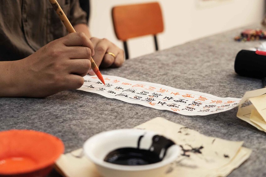 A person writing Chinese calligraphy on paper with a brush. 4