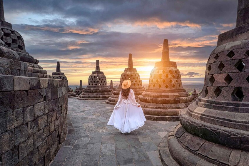 A person in a white dress walking on a stone pathway between ancient stone structures at sunset. 2