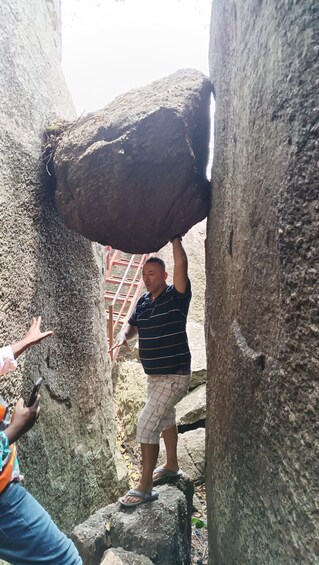 A person lifting a large rock in a rocky area with a ladder in the background. 3