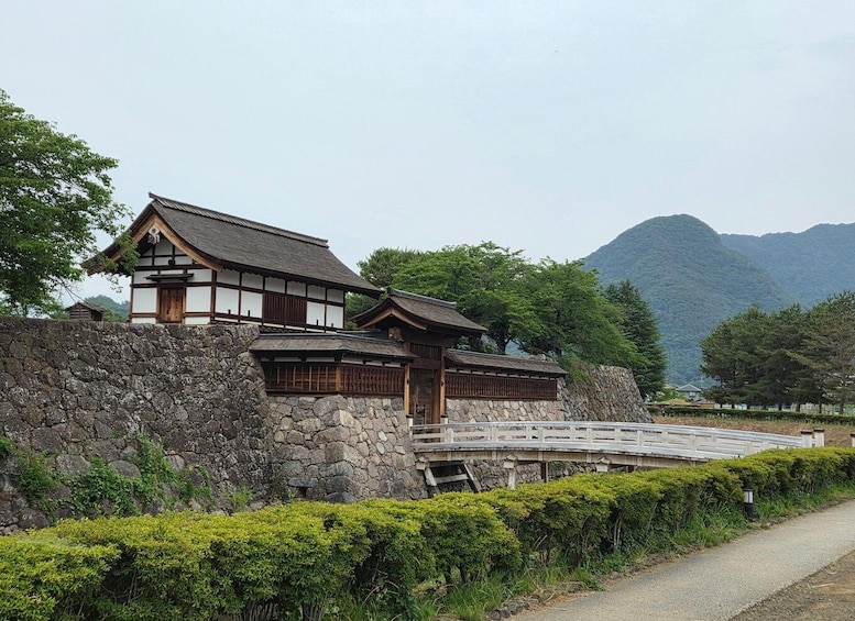 A traditional Japanese building with a stone wall and wooden gate, set against a mountainous backdrop. 3