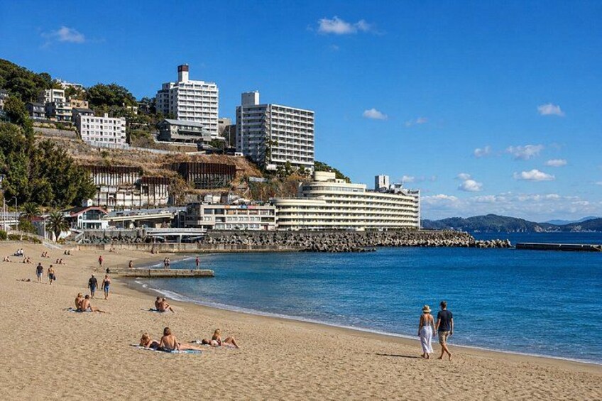A beach with people sunbathing, a pier, and buildings in the background. 3