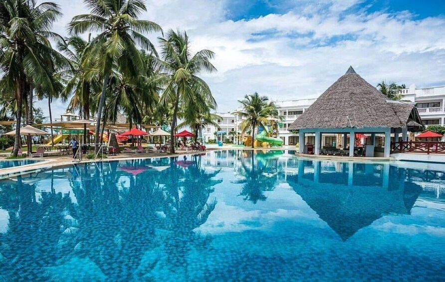 A clear blue pool surrounded by palm trees and a thatched-roof structure. 3
