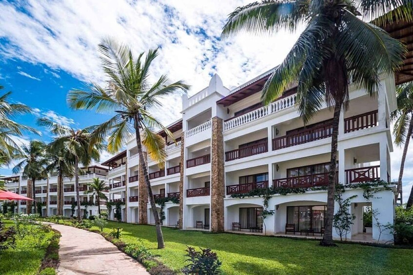 A multi-story hotel with balconies, surrounded by palm trees and a well-maintained lawn. 5