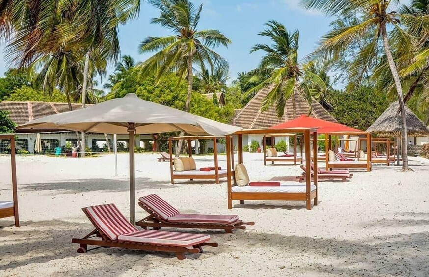 A beach with sun loungers, thatched-roof huts, and palm trees. 2