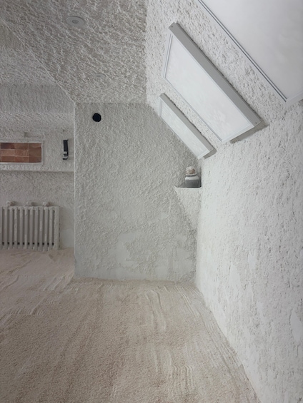 A room with textured white walls, a radiator, and a window with a wooden frame. 1
