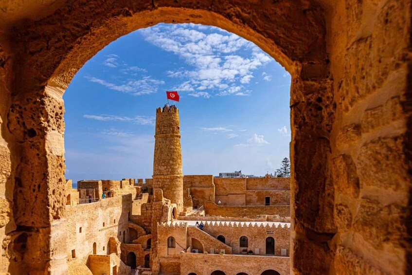A historic stone fortress with a prominent tower, a clear blue sky, and a flag atop the tower. 1