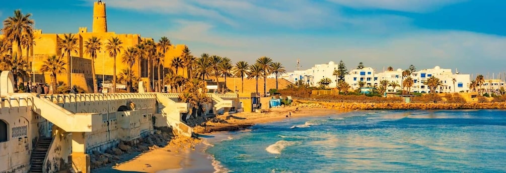 A coastal cityscape with a prominent historical tower, palm-lined promenade, and beachfront buildings. 4