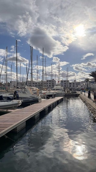 A marina with multiple sailboats docked along a wooden pier, under a partly cloudy sky. 5