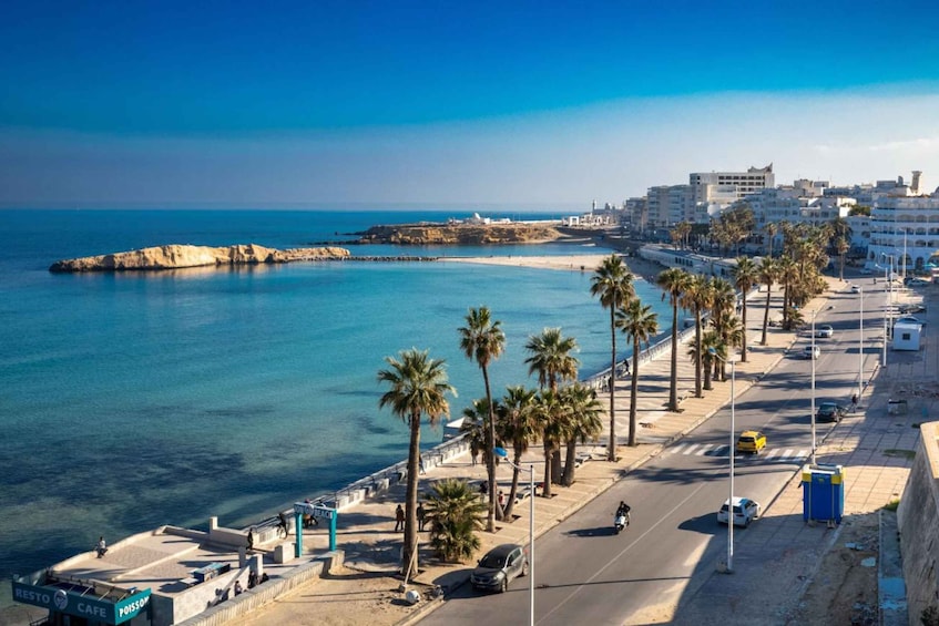 A coastal cityscape with a beach, palm trees, and a road with vehicles. 2