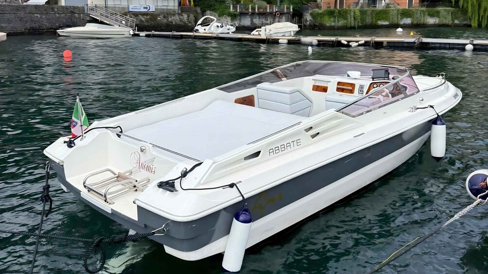 A white motorboat named 'ABBATE' docked at a marina with other boats and a stone wall in the background. 4