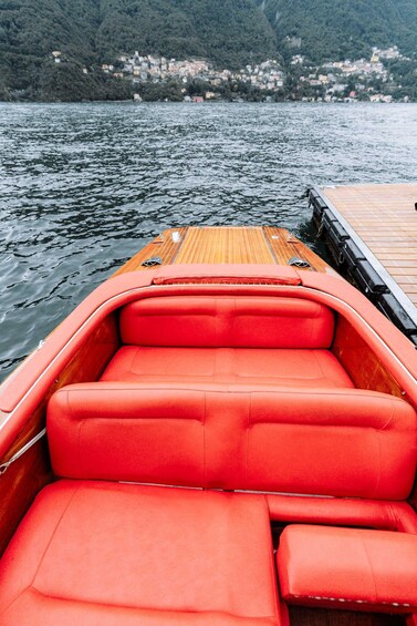 A boat with red seats and a wooden deck, docked at a pier with a mountainous backdrop. 3