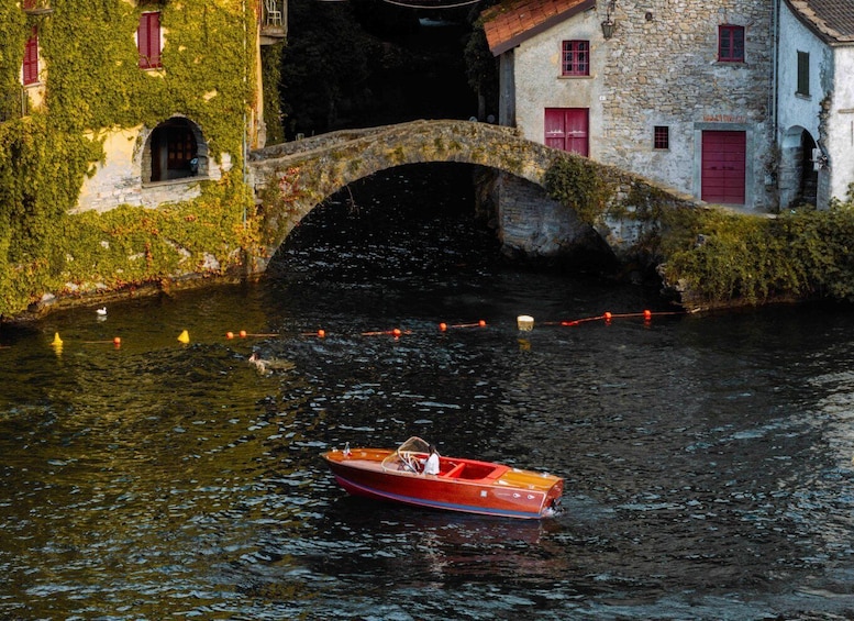 A narrow canal with a stone bridge, a red boat, and buildings covered in greenery. 2