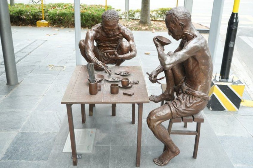 A bronze statue of two figures seated at a table with cooking utensils. 3