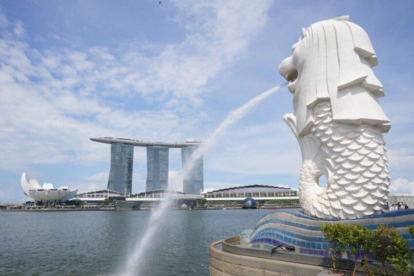 A large white lion statue, a water fountain, and the Marina Bay Sands hotel with its three towers. 1