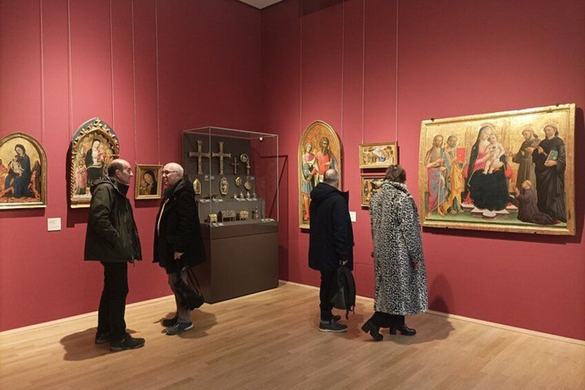 An art gallery with red walls and wooden floors. There are several paintings and a display case with religious artifacts. 5