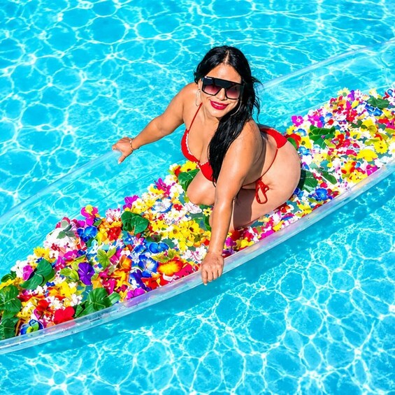 Una persona en traje de baño rojo sentada sobre una plataforma flotante en una piscina llena de flores artificiales de colores. 1