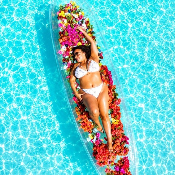 Una persona recostada sobre una plataforma flotante en una piscina rodeada de flores de colores. 4