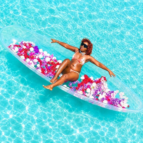 Una persona recostada sobre una plataforma flotante en una piscina, rodeada de flores de colores. 5