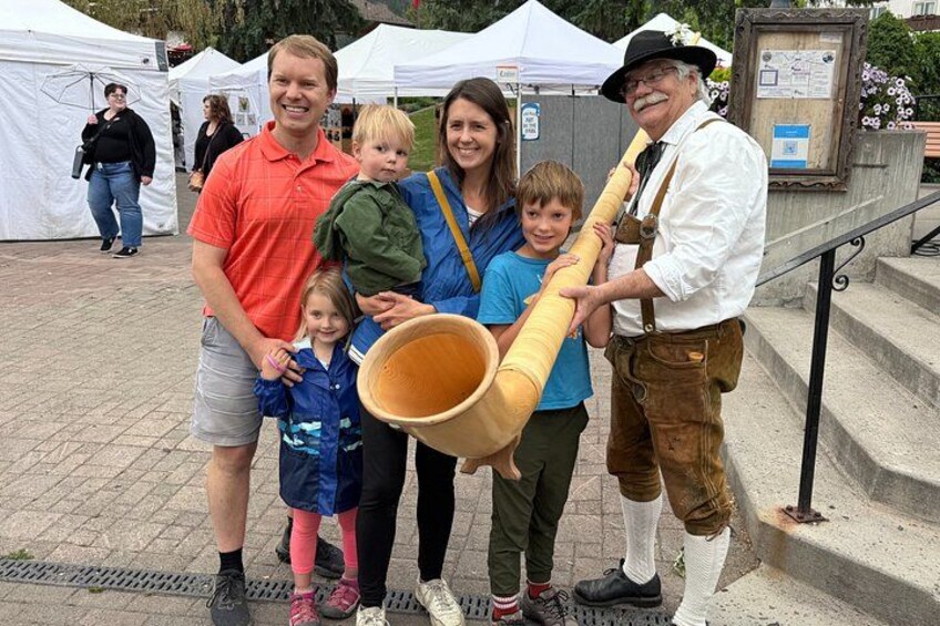 A family with a man in traditional attire holding a large drum, standing in front of a white tent. 5