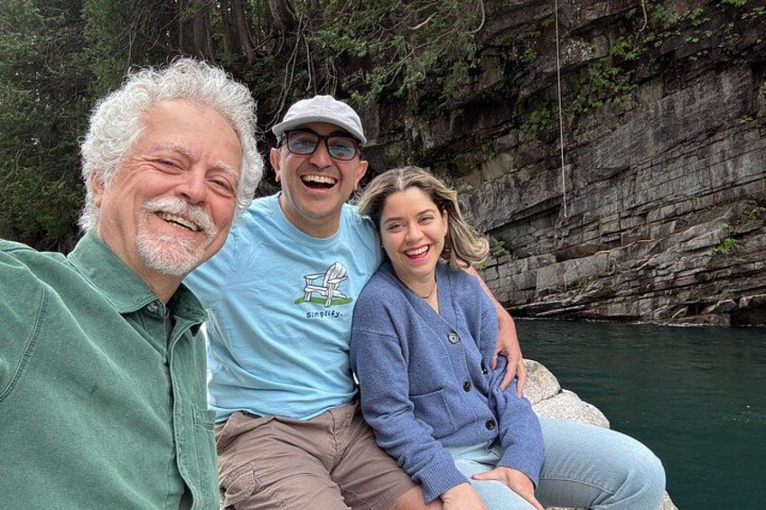 Three people sitting on a rock by a body of water with a rocky cliff in the background. 3