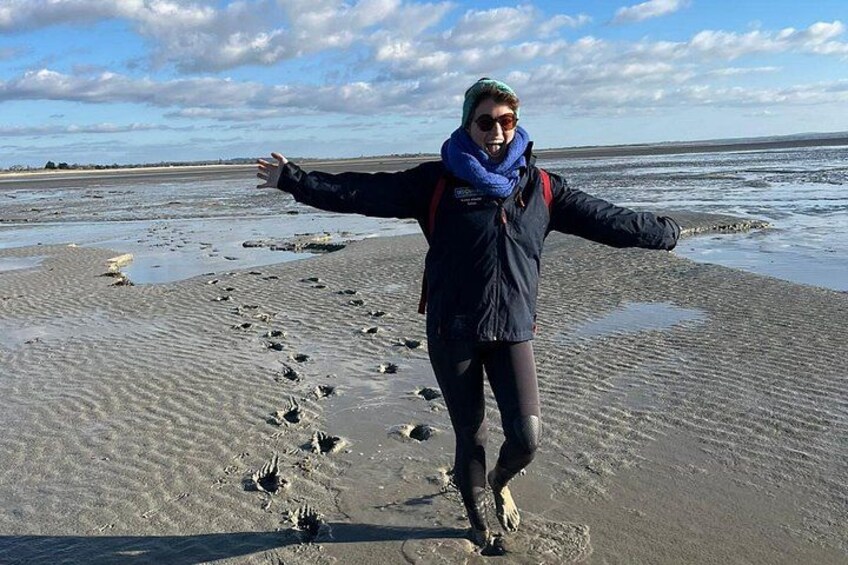 A person standing on a sandy beach with their arms outstretched, wearing a jacket and a scarf. 4