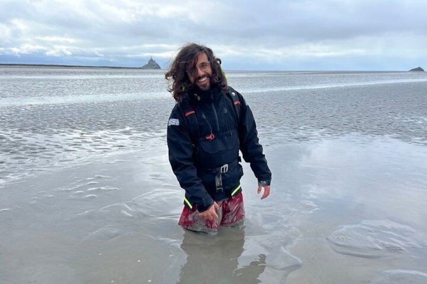 A person standing in shallow water on a beach with a cloudy sky in the background. 1