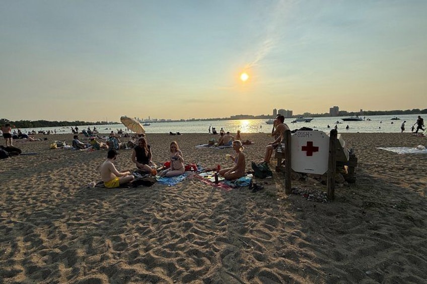 A beach with people sitting on towels, a lifeguard stand, and the sun setting over the water. 4