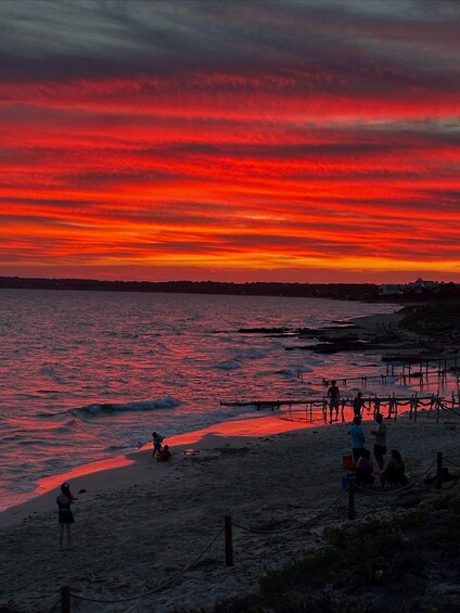 A sunset over a beach with people and a pier. 2