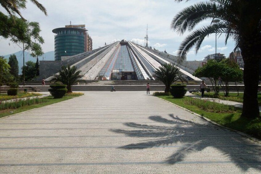 A wide, open plaza with a large, modern building with a triangular roof in the background. 2