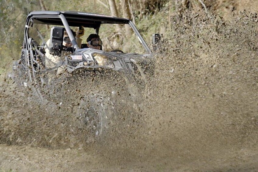 A vehicle driving through a muddy terrain, kicking up mud and water. 2