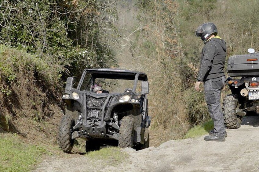 A person standing next to a quad bike on a dirt path with vegetation on the sides. 3