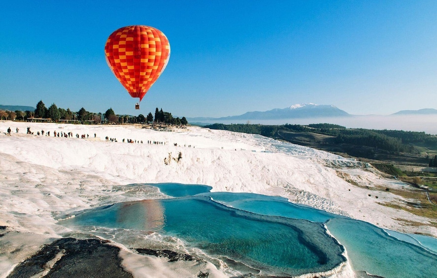 A hot air balloon over a geothermal area with mineral pools and a mountainous background. 3