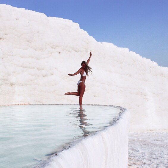 A person balancing on a ledge in a pool with a white, textured wall in the background. 3