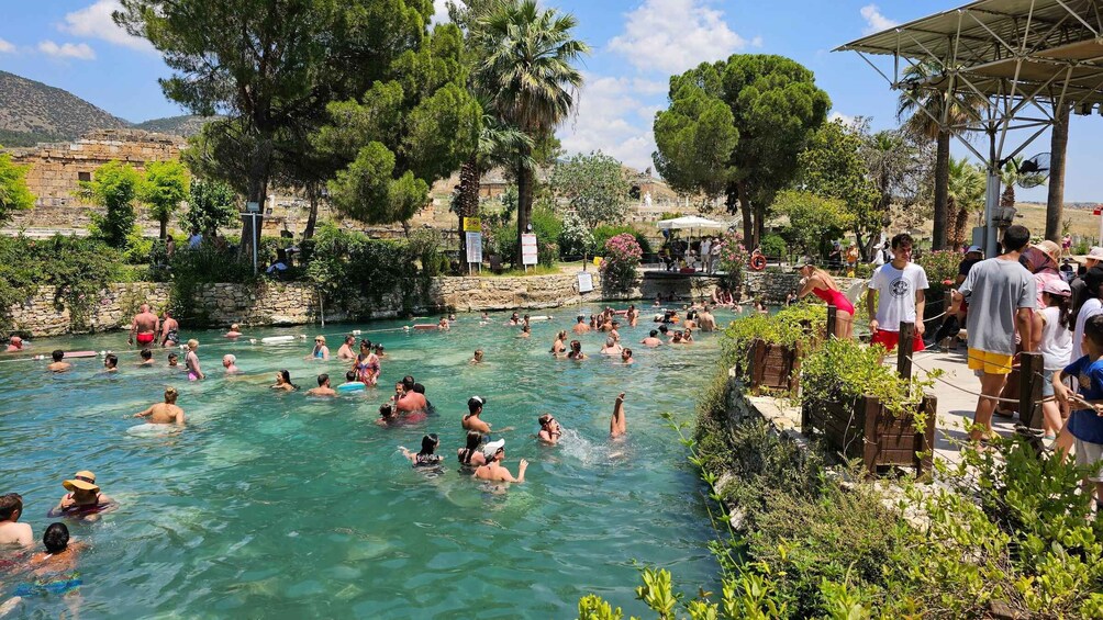 A crowded outdoor swimming pool surrounded by trees and a stone building. 5