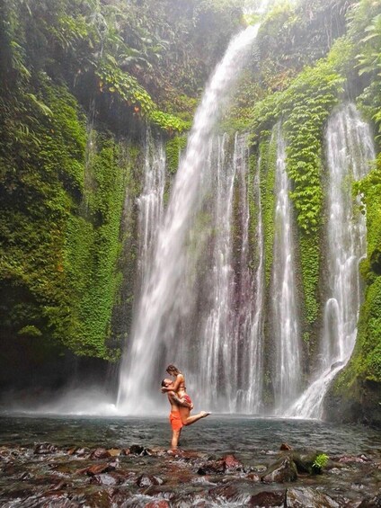 A waterfall with lush greenery and a person standing in the water. 5