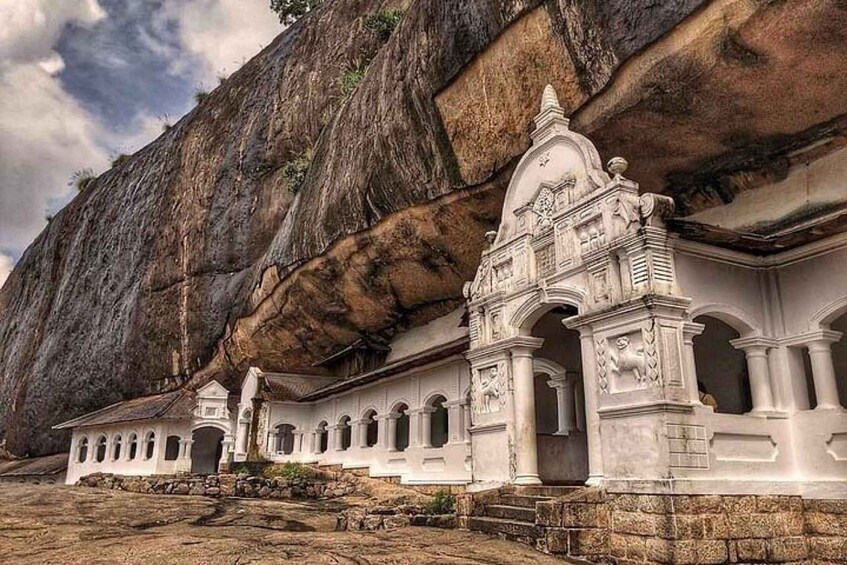A white temple with intricate carvings, set against a large rock formation. 4