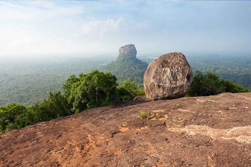 A large rock formation with a smaller peak in the distance, surrounded by dense forest. 5