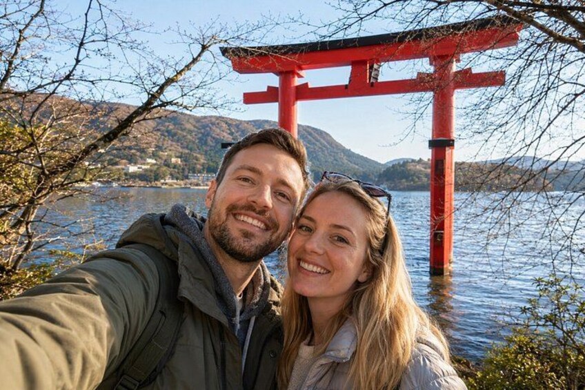 A couple taking a selfie with a red torii gate in the background and a lake. 1