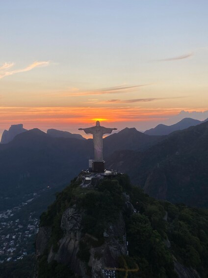 A statue on a mountain peak with a sunset in the background. 2