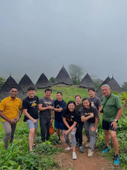 A group of people posing in front of traditional conical-roofed structures in a rural setting. 2