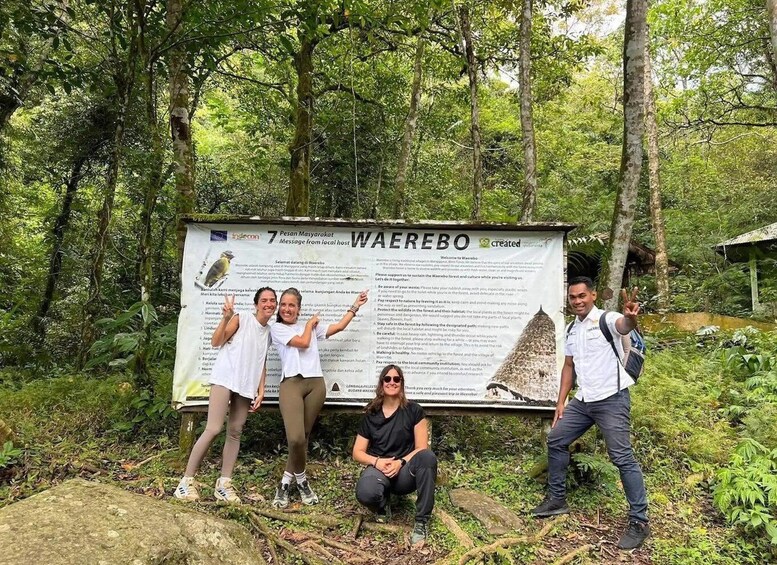 A group of people standing in front of a signboard in a forested area. 5