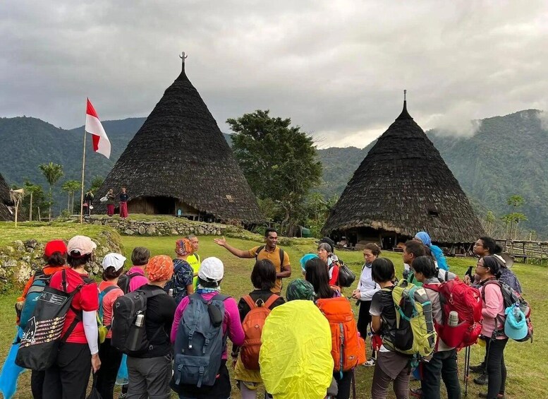 A group of hikers in front of traditional thatched-roof huts with a flag in the background. 3
