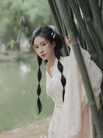 A person in traditional attire with braided hair, standing near bamboo structures by a body of water. 4