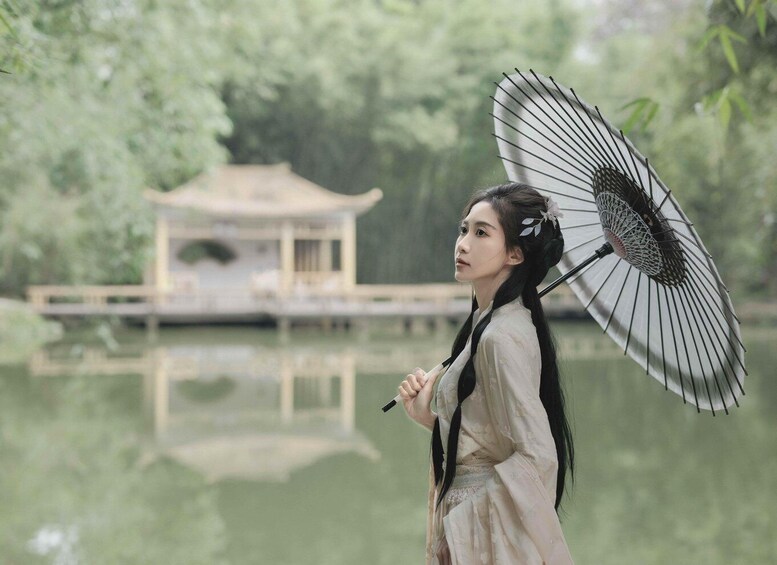 A person holding an umbrella in front of a traditional pavilion by a calm lake. 3