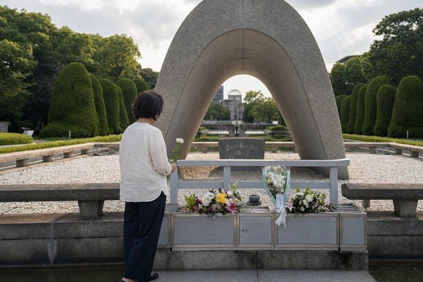 A person standing at a memorial with a curved stone arch, flowers, and a plaque. 3