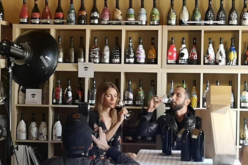 Two people tasting wine in a room with shelves of wine bottles. 3