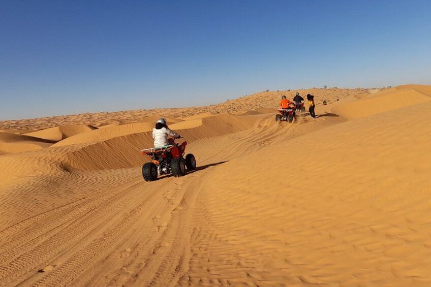 A desert landscape with sand dunes and a person riding a quad bike. 2