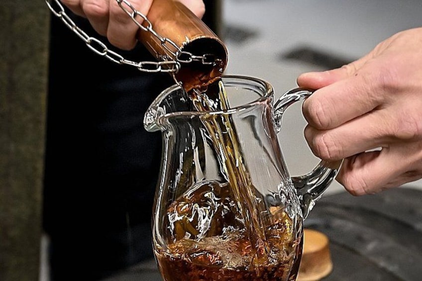 A person pouring a dark liquid from a copper container into a glass pitcher. 4