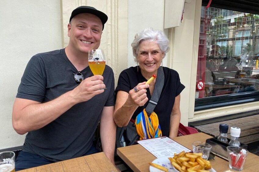 Two people sitting at a table with a meal, one holding a glass of beer. 2