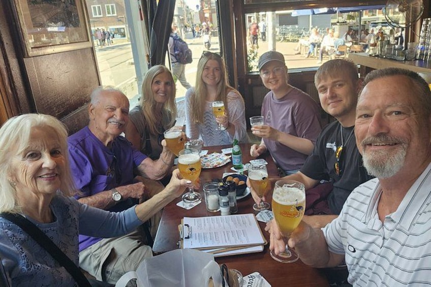A group of people sitting at a table, holding glasses of beer, with a menu and a bottle on the table. 5